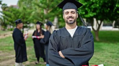 Bir grup öğrenci üniversite kampüsünde kollarını kavuşturarak diploma alarak mezun oldular.