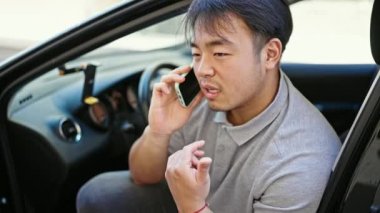 Akıllı telefondan konuşuyor. Sokakta arabada oturuyor.