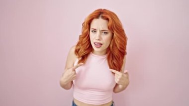 Genç kızıl saçlı kadın kendini göstererek hayır diyor. Parmak izole edilmiş pembe arka planda gülümsüyor.