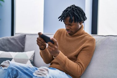 Evdeki kanepede oturan Afrikalı Amerikalı bir adam video oyunu oynuyor.