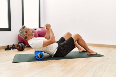 Spor merkezinde gerinirken köpük paten kullanan orta yaşlı, kır saçlı bir adam.