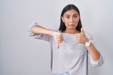 Young hispanic woman standing over white background doing thumbs up and down, disagreement and agreement expression. crazy conflict 