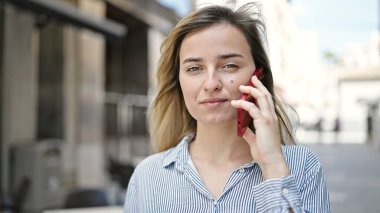 Kahve dükkanının terasında akıllı telefondan konuşan genç sarışın kadın.