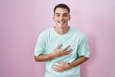 Pembe arka planda duran yakışıklı İspanyol adam. Gülümsüyor ve kahkahalar atıyor. Çünkü elleri vücutta komik, çılgın bir şaka.. 