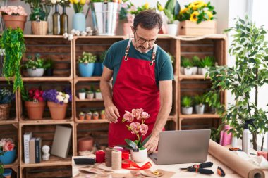 Çiçekçide dizüstü bilgisayar kullanan orta yaşlı bir çiçekçi.