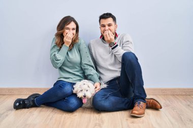 Genç İspanyol bir çift yerde oturmuş köpeğiyle gülüyor ve utanıyor kıkırdıyor ağızlarını ellerle kapatıyor, dedikodu yapıyor ve skandal konsepti yapıyor. 