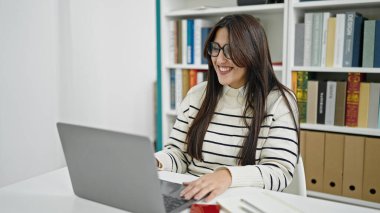 Kütüphanede gülümseyen dizüstü bilgisayar kullanan güzel İspanyol bir kız öğrenci.