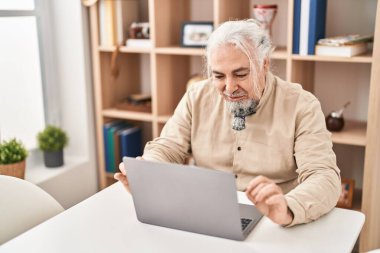 Middle age grey-haired man having video call sitting on table at home