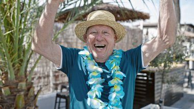 Kıdemli gri saçlı turist yaz şapkası takıyor ve Hawai leyleği sokak tabiriyle ayakta duruyor.