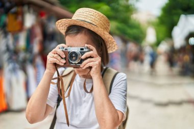 Sokak pazarında klasik kamera kullanan orta yaşlı bir turist.
