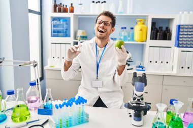 Laboratuvarda çalışan Latin asıllı genç bir adam elma tutuyor ve kahkahalarla gülüyor.. 