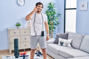 Evde spor giyinen yakışıklı Latin adam gülümsüyor telefonla el ve parmaklarıyla jest yapıyor telefonda konuşuyor gibi. iletişim kavramları. 