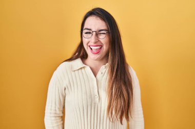Young hispanic woman standing over yellow background winking looking at the camera with sexy expression, cheerful and happy face. 