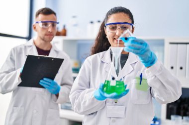 Man and woman wearing scientist uniform write on document measuring liquid at laboratory