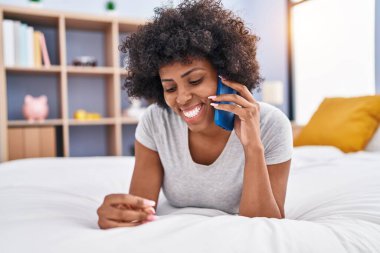 African american woman talking on smartphone lying on bed at bedroom