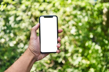 Akıllı telefonu tutan adam parkta beyaz ekranı gösteriyor.