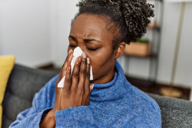 Afro-Amerikalı kadın evdeki kanepede peçete kullanıyor.