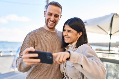 Man and woman couple smiling confident using smartphone at seaside