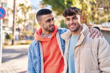 Two man couple hugging each other standing at park