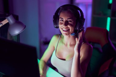 Young beautiful hispanic woman streamer playing video game using computer at gaming room