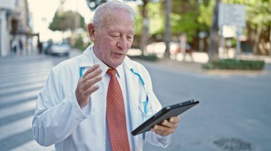 Kıdemli gri saçlı adam doktor gülümsüyor. Sokaktan video çağrısı geliyor.