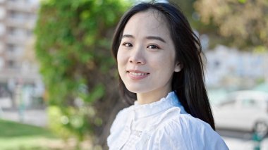 Parkta kendinden emin gülümseyen genç Çinli kadın.