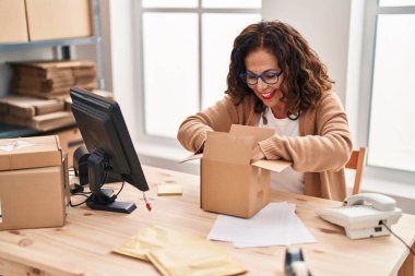 Middle age hispanic woman working packing a box at ecommerce