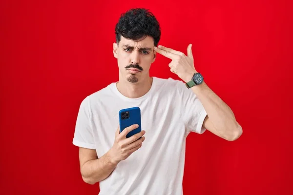 Hispanic Man Using Smartphone Red Background Shooting Killing Oneself Pointing — Stock Photo, Image