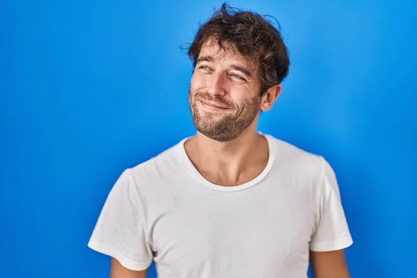 Іспанський Молодий Чоловік Стоїть Над Синім Фоном Посміхається Дивлячись Убік — стокове фото