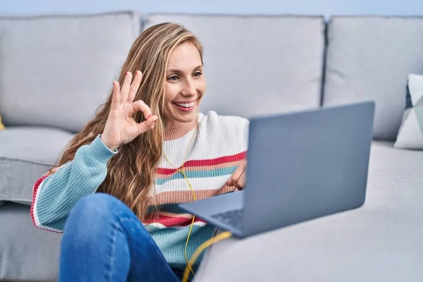 Молода Блондинка Використовуючи Ноутбук Вдома Робить Знак Пальцями Посміхаючись Дружній — стокове фото