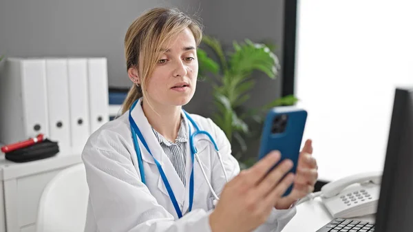 年轻的金发女医生用智能手机在诊所工作 — 图库照片