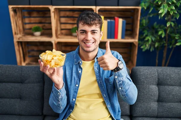 Young Hispanic Man Holding Potato Chips Smiling Happy Positive Thumb — Stock Photo, Image