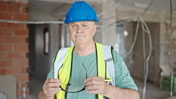 中年人灰白头发的建筑工人站在建筑工地 手里拿着一副眼镜 一副轻松的表情 — 图库照片