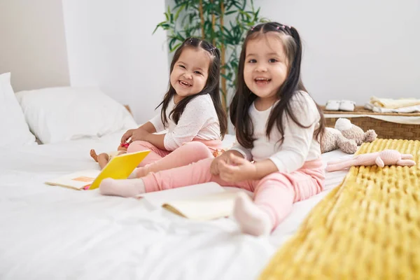 ベッドルームでベッドの上に座っているノートブックに描かれた愛らしい双子の女の子 — ストック写真