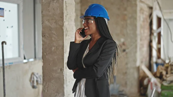 アフリカ系アメリカ人の女性建築家が建設現場でスマートフォンで自信を持って話しています — ストック写真