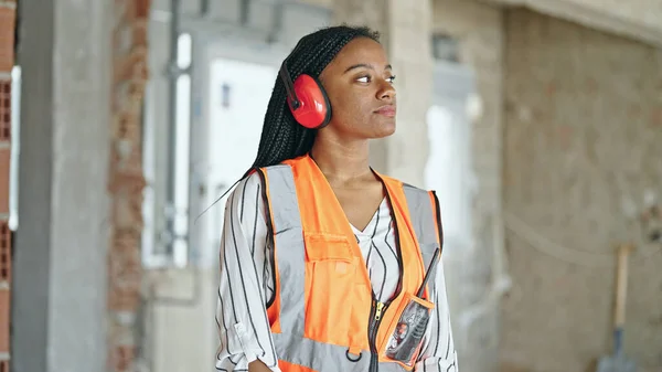 建設現場での騒音のためのヘッドフォンを身に着けているアフリカ系アメリカ人女性ビルダー — ストック写真
