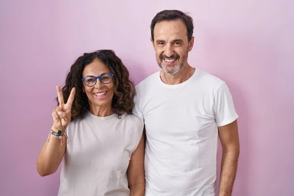 Middelbare Leeftijd Hispanic Paar Samen Roze Achtergrond Tonen Wijzen Met — Stockfoto
