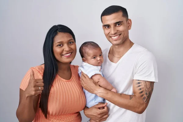 赤ちゃんが孤立した背景の上に一緒に立っている若いヒスパニック系のカップルは 手で幸せな親指アップジェスチャーを行います 成功を示すカメラを見ると — ストック写真