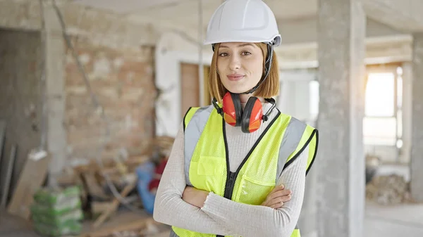 年轻的金发女建筑师微笑着自信地站在建筑工地上 双手交叉地做着手势 — 图库照片