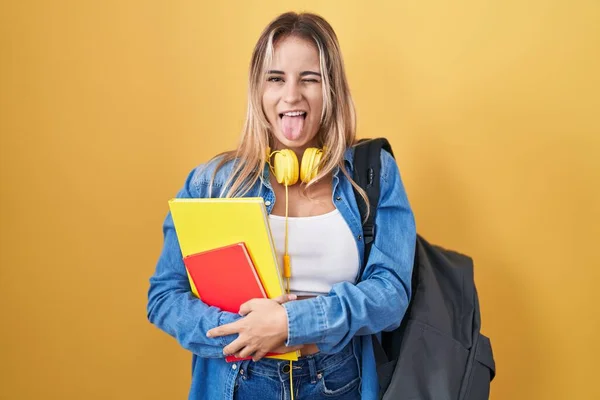 学生用バックパックを身に着けている若いブロンドの女性と面白い表情で幸せ舌を突き出す本を保持 感情の概念 — ストック写真