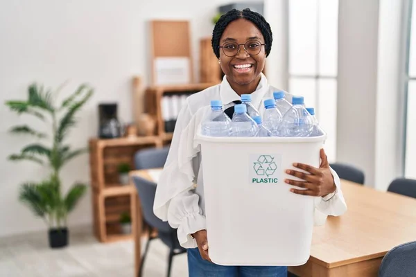 アフリカ系アメリカ人の女性がオフィスで働いているので 笑顔をリサイクルし 大声で笑いのためのプラスチックボトルを保持面白いクレイジー冗談 — ストック写真