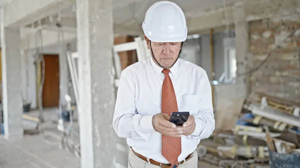 建設現場を見回すスマートフォンを使用したシニア白髪の男建築家 — ストック写真