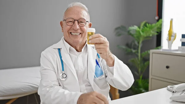 Senior Gråhåret Mand Læge Holder Piller Sidder Bordet Klinikken - Stock-foto