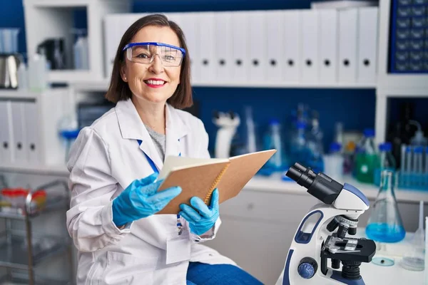 Mulher Meia Idade Cientista Sorrindo Livro Leitura Confiante Laboratório — Fotografia de Stock