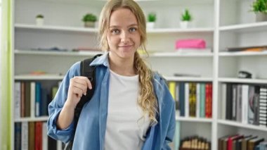 Kütüphanede sırtüstü sırtüstü gülümseyen sarışın bir kız öğrenci.