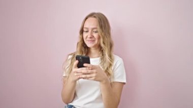 Akıllı telefon kullanan genç sarışın kadın pembe arka planda gülümsüyor.