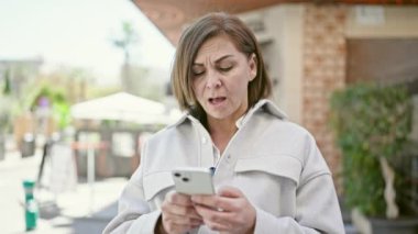 Orta yaşlı İspanyol kadın sokakta akıllı telefon kullanıyor.