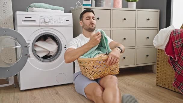 Ung Latinamerikansk Man Sitter Golvet Trött Håller Korg Med Kläder — Stockvideo