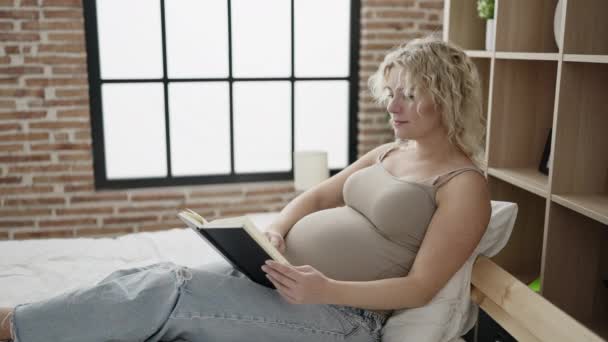 Молодая Беременная Женщина Читает Книгу Касаясь Живота Спальне — стоковое видео