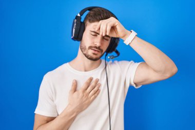 Sakallı İspanyol adam kulaklık takıyor hastalık, ateş, grip ve virüs için alnına dokunuyor. 